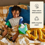 Young boy sits up in bed playing with toys with a box of Who Gives a Crap toilet paper beside him. Callout text reads ‘Helps reduce deforestation’ and ‘100% recycled paper’.