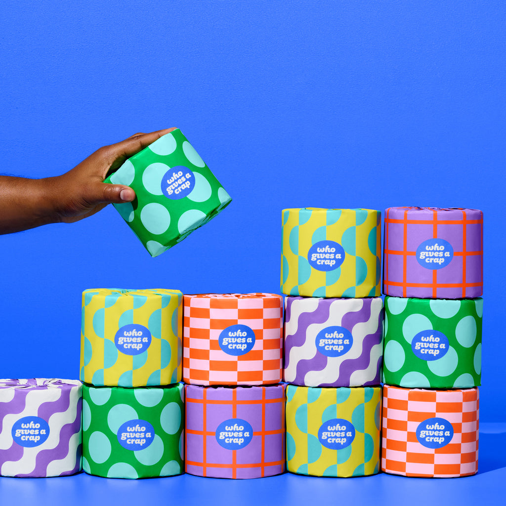 Recycled Toilet Paper in colourful packaging with a hand lifting up one roll of toilet paper