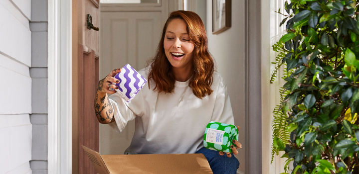 Woman collecting box of Who Gives a Crap toilet paper from front porch of home smiles as she opens box